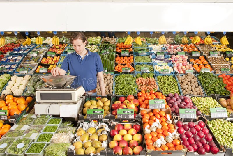 A green grocer weighing vegetables in a grocery shop. A green grocer weighing vegetables in a grocery shop