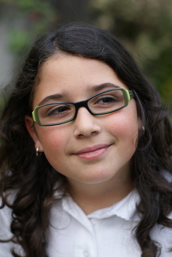 A young girl smiling outdoors wearing green glasses. A young girl smiling outdoors wearing green glasses