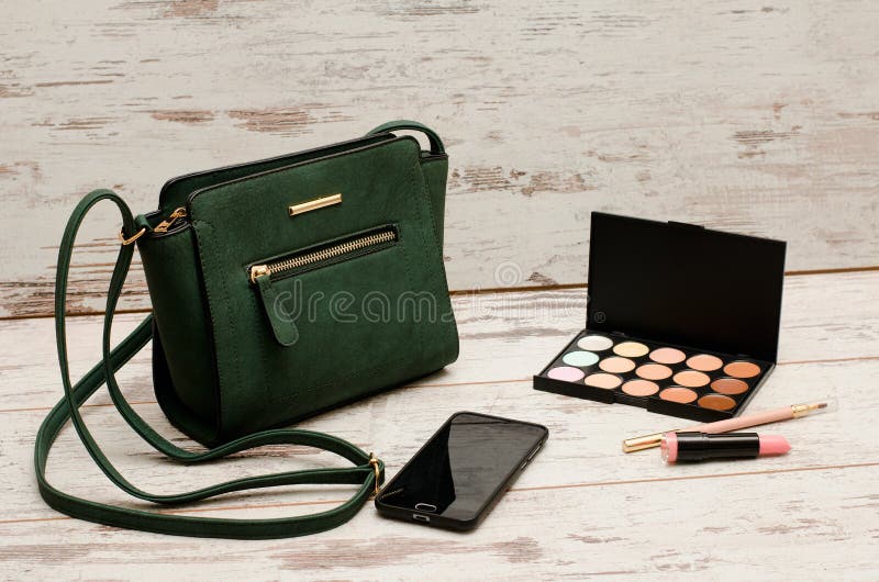 Grüne Damen Handtasche, Telefon, Lidschattenpalette und ein Lippenstift auf einem hölzernen Hintergrund stockfoto Grüne Damen Handtasche, Telefon, Lidschattenpalette und ein Lippenstift auf einem hölzernen Hintergrund stockfoto