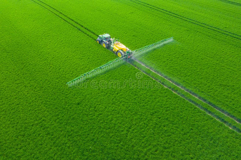 Green Fields. Aerial view of the tractor spraying the chemicals on the large green field. Agricultural spring background. Green Fields. Aerial view of the tractor spraying the chemicals on the large green field. Agricultural spring background.