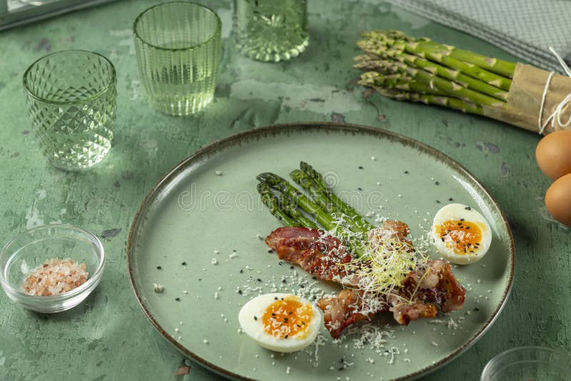 Grüner Spargel mit gebratenen Eiern aus Speck und Parmesan-Käse auf dem Teller stockfotografie