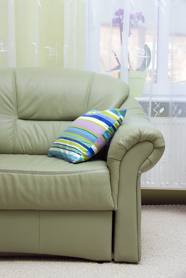 A green leather sofa and a striped pillow - living room interior. A green leather sofa and a striped pillow - living room interior.