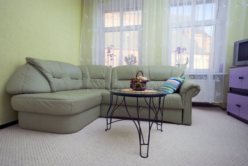 A green sofa and a pillow - living room interior. Wide angle, TV and cupboards in the corner. A green sofa and a pillow - living room interior. Wide angle, TV and cupboards in the corner.