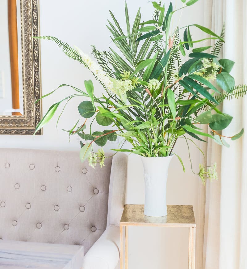 Grünes tropisches Houseplantsbündel im Vase nahe der Couch im Luxuswohnzimmer Glaskerzen, Oberteile und Anlagen stockfotografie Grünes tropisches Houseplantsbündel im Vase nahe der Couch im Luxuswohnzimmer Glaskerzen, Oberteile und Anlagen stockfotografie