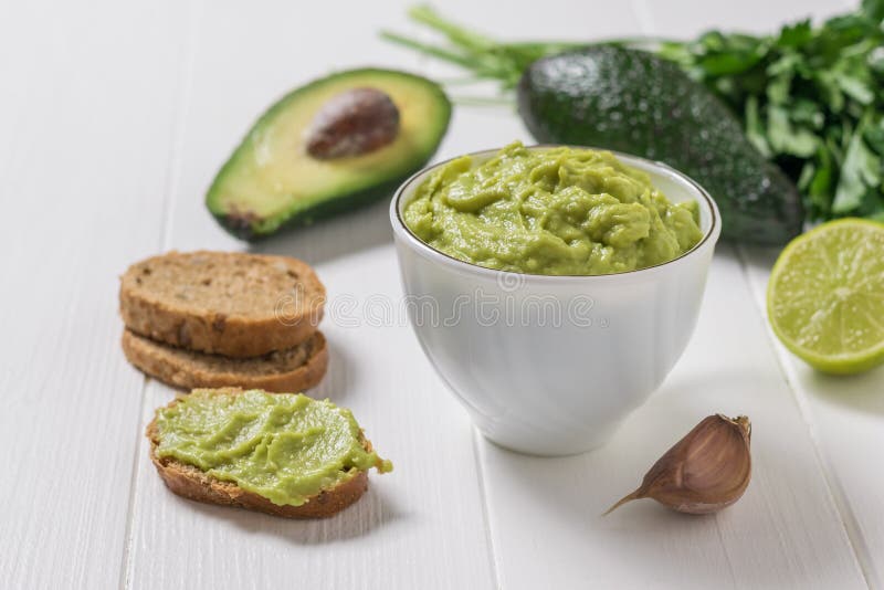 Guacamole fresco in una coppa bianca e a fette di pane Avocado alimentare vegetariano messicano dietetico immagini stock