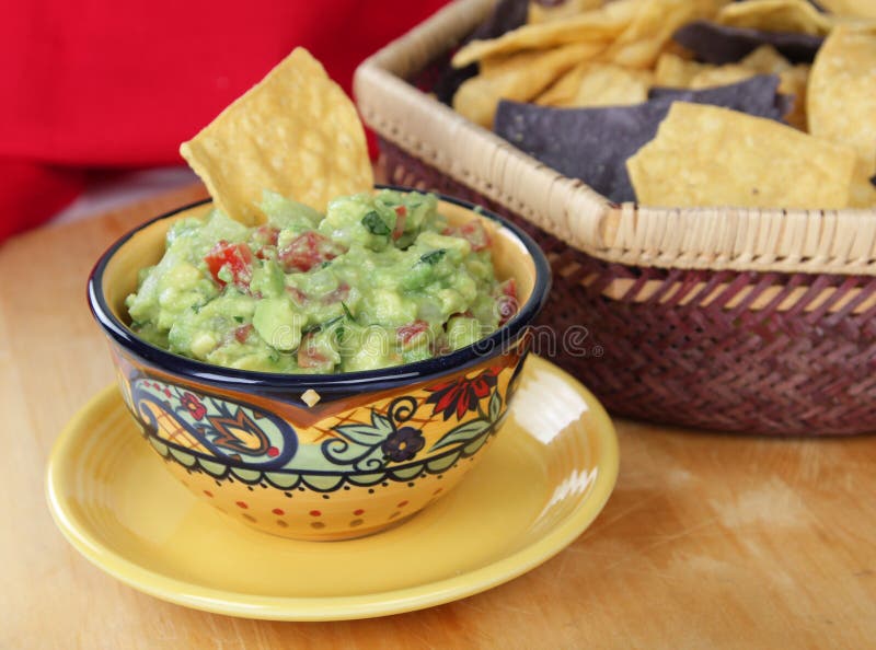 Bowl of guacamole dip with basket of tortilla chips. Bowl of guacamole dip with basket of tortilla chips.