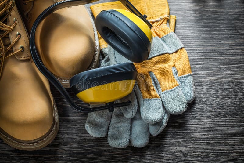 Guantes de la seguridad que trabajan orejeras de las botas en el tablero de madera imagen de archivo Guantes de la seguridad que trabajan orejeras de las botas en el tablero de madera imagen de archivo