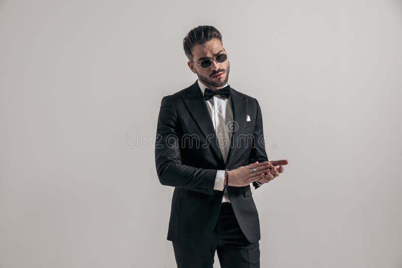 Guapo tipo sin afeitar vestido con elegante esmoquin frotando las palmas imagen de archivo