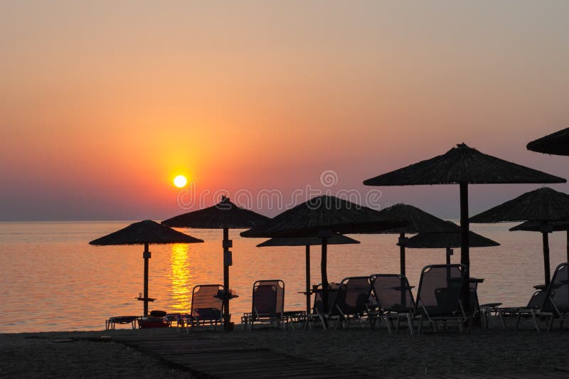 Guarda-chuvas de praia no por do sol, com sunbeds, por do sol quente na praia imagem de stock Guarda-chuvas de praia no por do sol, com sunbeds, por do sol quente na praia imagem de stock