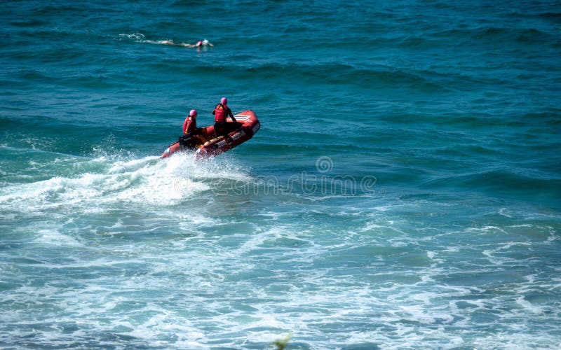 Guardabosques de la playa en un bote de salvamento rojo una persona que practica surf que nada cerca imágenes de archivo libres de regalías Guardabosques de la playa en un bote de salvamento rojo una persona que practica surf que nada cerca imágenes de archivo libres de regalías