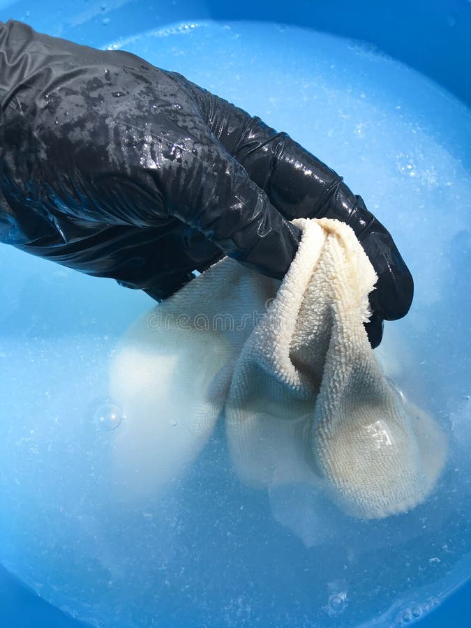 In a blue basin wash a multi-colored napkin with a female hand in black gloves. In a blue basin wash a multi-colored napkin with a female hand in black gloves