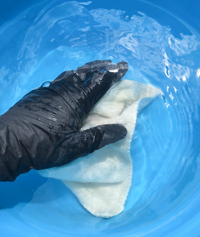 In a blue basin wash a multi-colored napkin with a female hand in black gloves. In a blue basin wash a multi-colored napkin with a female hand in black gloves