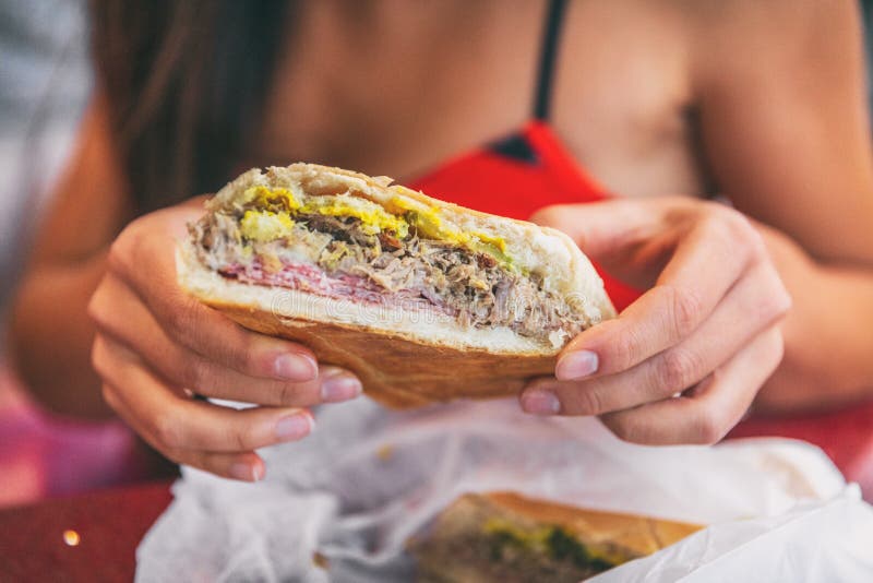 Cuban sandwich closeup woman holding local food at typical cafe outside. Pressed cuban bread with roasted pork, salami sausage, swiss cheese, mustard, typical cuba dish. Cuban sandwich closeup woman holding local food at typical cafe outside. Pressed cuban bread with roasted pork, salami sausage, swiss cheese, mustard, typical cuba dish.