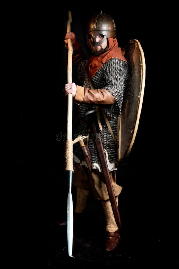 Guerreiro farpado na armadura e no capacete das posses de Viking Age um protetor, uma espada, um machado e uma lança fotos de stock Guerreiro farpado na armadura e no capacete das posses de Viking Age um protetor, uma espada, um machado e uma lança fotos de stock