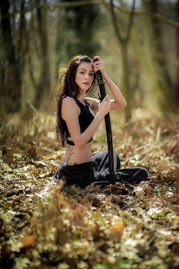 Guerrier de femme tenant Katana Sword, dans la forêt mystique photographie stock libre de droits Guerrier de femme tenant Katana Sword, dans la forêt mystique photographie stock libre de droits