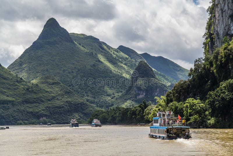 Guilin, Κίνα - τον Ιούλιο του 2015 circa: Πανιά βαρκών κρουαζιέρας μεταξύ των βουνών καρστ και των αιχμών ασβεστόλιθων του ποταμο στοκ εικόνα με δικαίωμα ελεύθερης χρήσης Guilin, Κίνα - τον Ιούλιο του 2015 circa: Πανιά βαρκών κρουαζιέρας μεταξύ των βουνών καρστ και των αιχμών ασβεστόλιθων του ποταμο στοκ εικόνα με δικαίωμα ελεύθερης χρήσης