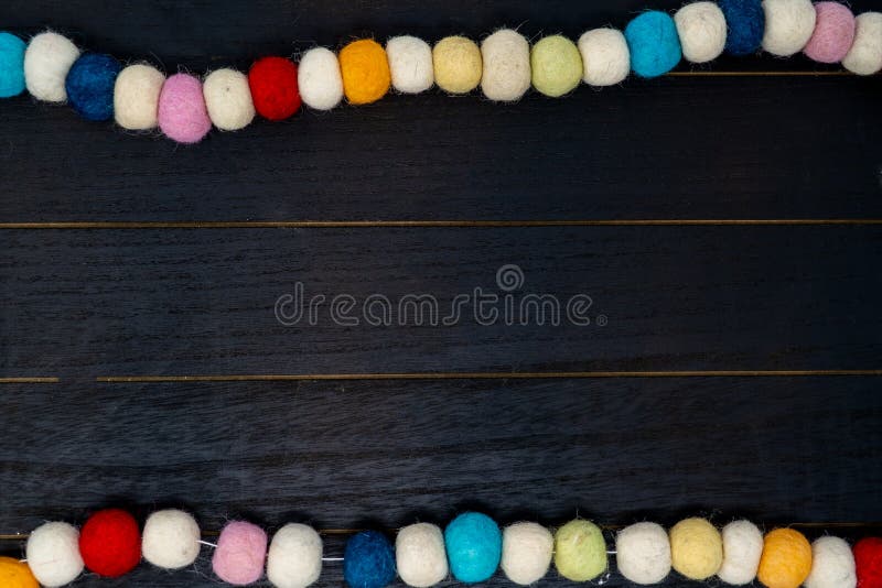 Guirnalda colorida bonita de la tela del pom del pom del arco iris sobre fondo de madera negro imágenes de archivo libres de regalías Guirnalda colorida bonita de la tela del pom del pom del arco iris sobre fondo de madera negro imágenes de archivo libres de regalías