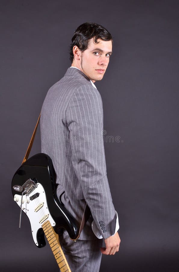 Muž v pruhovanom oblek s elektrickou gitarou pri pohľade cez rameno.