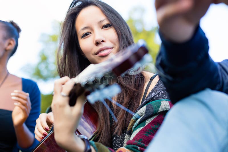 Guitar player girl making music with friends in park