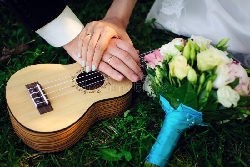 Guitar, wedding bouquet and hands of the newlyweds, close-up. Ukulele, hands of the bride and groom with wedding rings