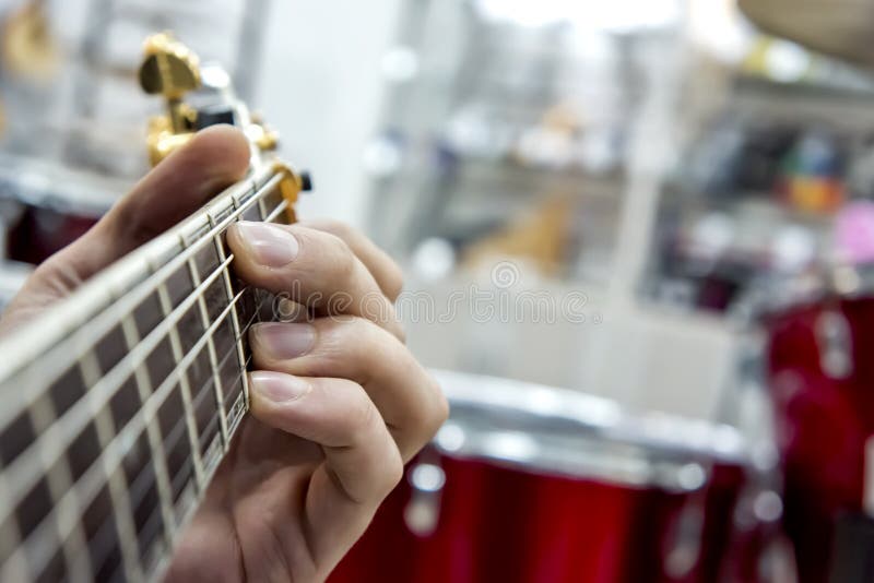 The guitarist`s hand, close-up and soft focus, takes the akrod on a guitar fretboard, against the background of the drum set. Performance, isolated.