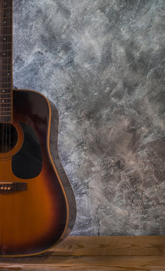 Guitarra acústica que descansa contra na tabela de madeira uma parede vazia do cimento imagens de stock Guitarra acústica que descansa contra na tabela de madeira uma parede vazia do cimento imagens de stock