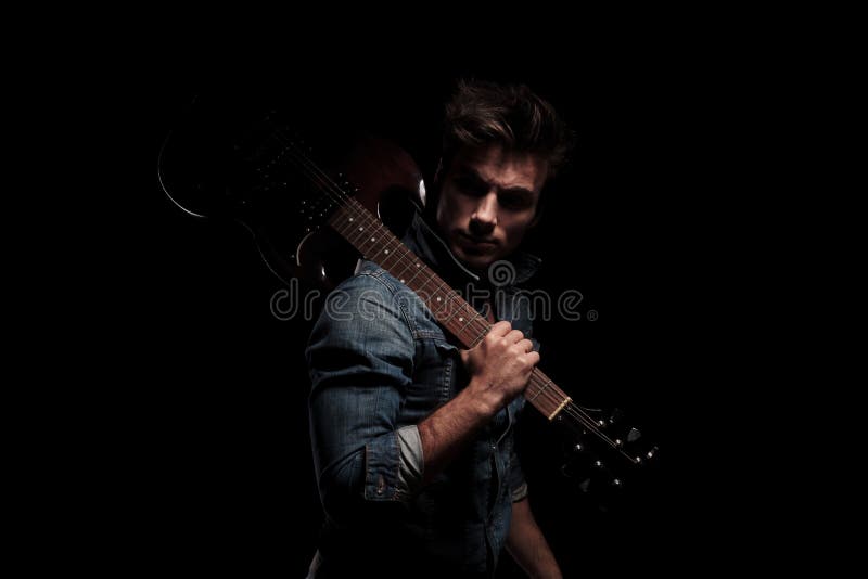 Guitarrista novo dramático que olha para trás ao guardar a guitarra em sh imagens de stock Guitarrista novo dramático que olha para trás ao guardar a guitarra em sh imagens de stock