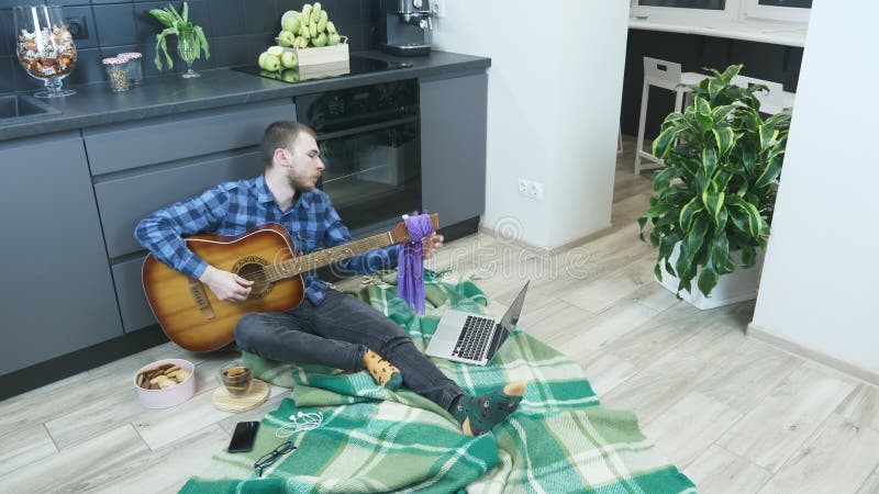 Guitarrista profissional que toca guitarra sentada no chão da cozinha em casa. músico tunista guitarra em casa durante a quarenten