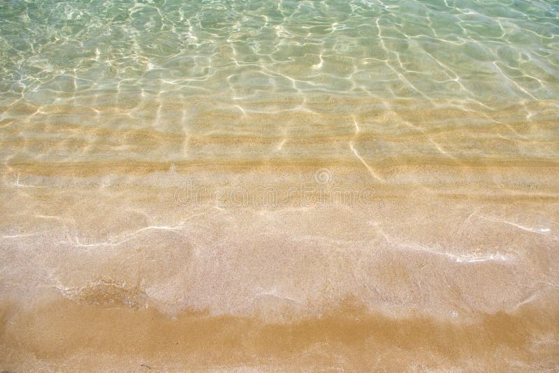 Guld- sand och genomskinligt vatten, textur arkivbilder