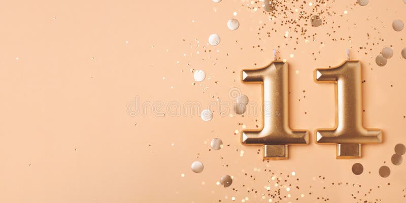 Gold candles in the form of number eleven on peach background with confetti. 11 years celebration. Gold candles in the form of number eleven on peach background with confetti. 11 years celebration.