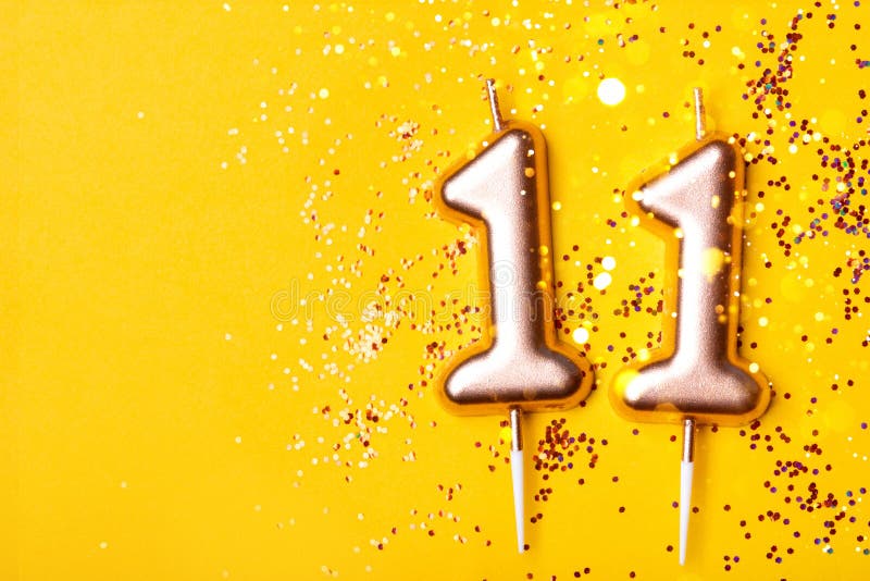 Gold candles in the form of number eleven on yellow background with confetti. 11 years celebration. Gold candles in the form of number eleven on yellow background with confetti. 11 years celebration.