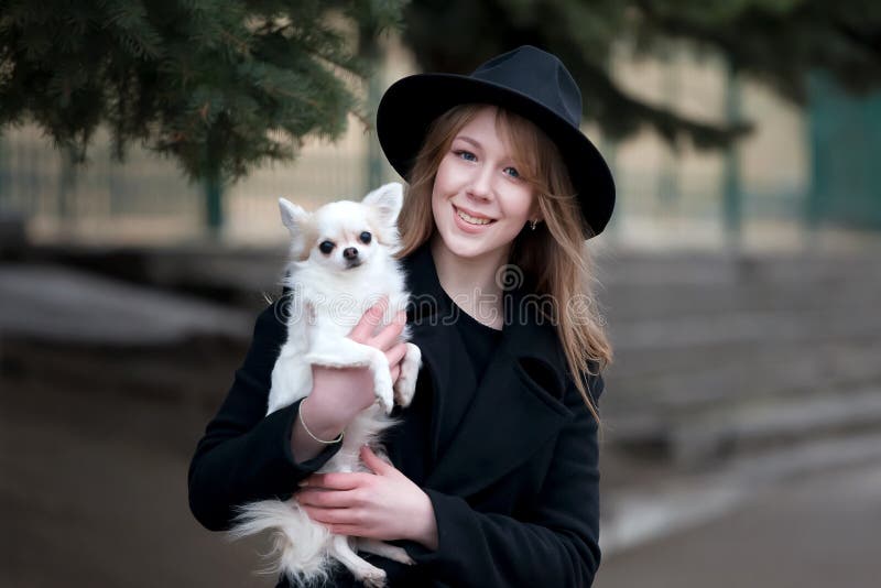Gullig gladlynt slank caucasian flickablondin med långt hår i ett svart lag och en svart hatt in i höstdagen med hennes vita lite royaltyfri fotografi Gullig gladlynt slank caucasian flickablondin med långt hår i ett svart lag och en svart hatt in i höstdagen med hennes vita lite royaltyfri fotografi