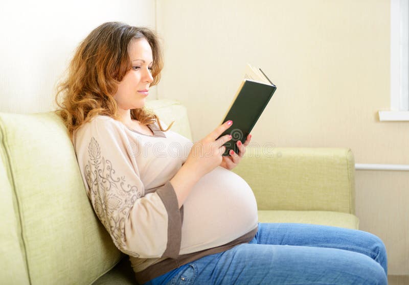 Gullig gravid kvinna som hemma läser en bok royaltyfria bilder Gullig gravid kvinna som hemma läser en bok royaltyfria bilder