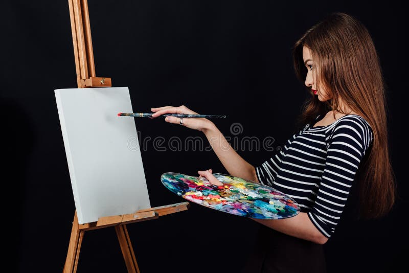 Gullig härlig flickakonstnär som målar en bild på kanfas en staffli Utrymme för text Svart bakgrund för studio royaltyfri fotografi Gullig härlig flickakonstnär som målar en bild på kanfas en staffli Utrymme för text Svart bakgrund för studio royaltyfri fotografi
