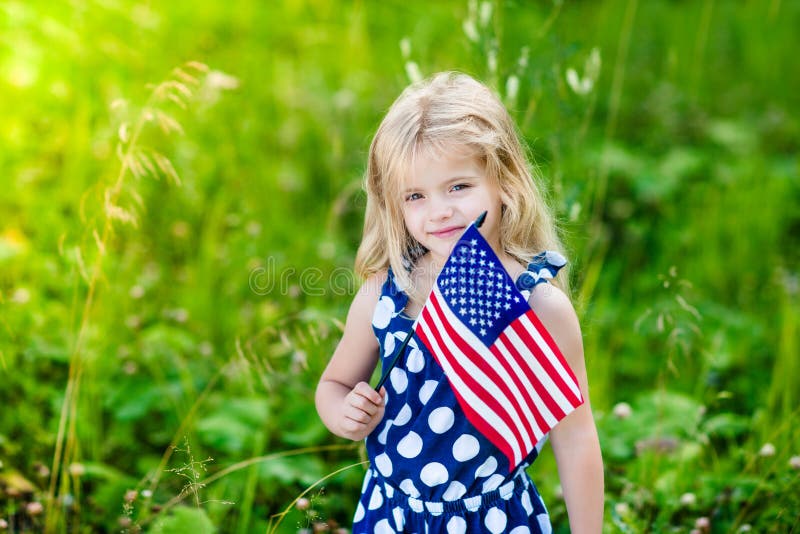 Gullig le liten flicka med den hållande amerikanska flaggan för blont hår arkivfoto Gullig le liten flicka med den hållande amerikanska flaggan för blont hår arkivfoto