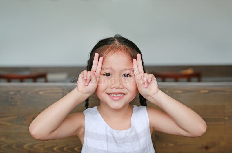 Gullig liten asiatisk flicka med uttryck som kanin som ligger på trätabellen med att se kameran royaltyfri foto Gullig liten asiatisk flicka med uttryck som kanin som ligger på trätabellen med att se kameran royaltyfri foto
