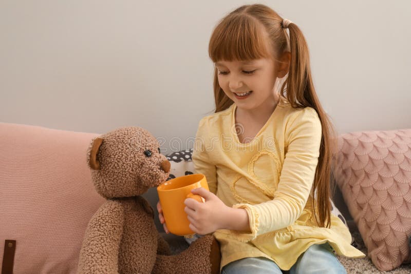 Gullig liten flicka som hemma behandlar leksakbjörnen med koppen av den varma kakaodrinken arkivfoto Gullig liten flicka som hemma behandlar leksakbjörnen med koppen av den varma kakaodrinken arkivfoto