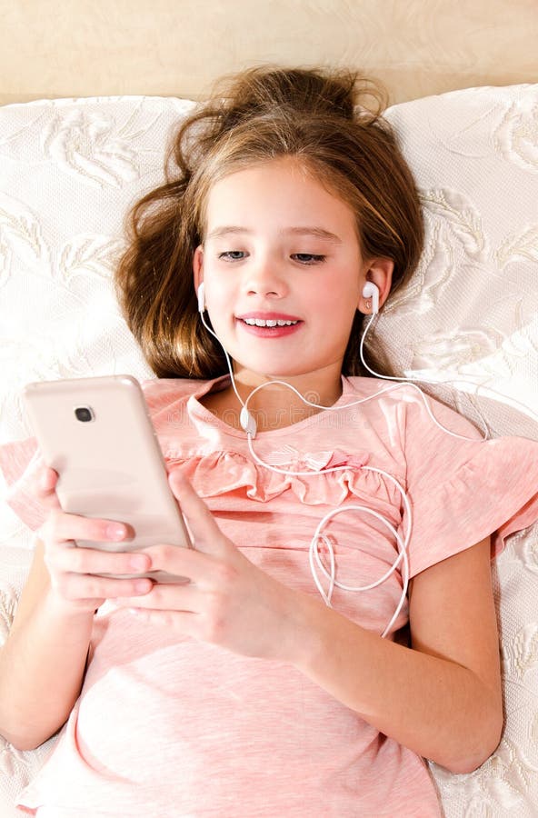 Gullig liten flicka som ligger på sängen och lyssnar till musik genom att använda s royaltyfri bild Gullig liten flicka som ligger på sängen och lyssnar till musik genom att använda s royaltyfri bild