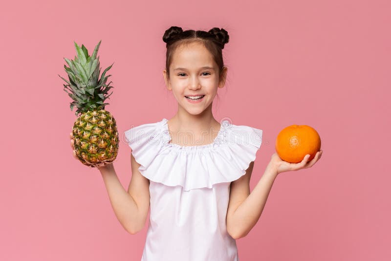 Gullig liten flicka som rymmer den nya ananas och apelsinen arkivbild Gullig liten flicka som rymmer den nya ananas och apelsinen arkivbild