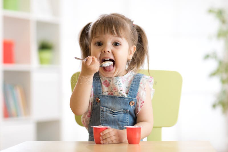 Cute little child girl eating yogurt indoors. Cute little child girl eating yogurt indoors