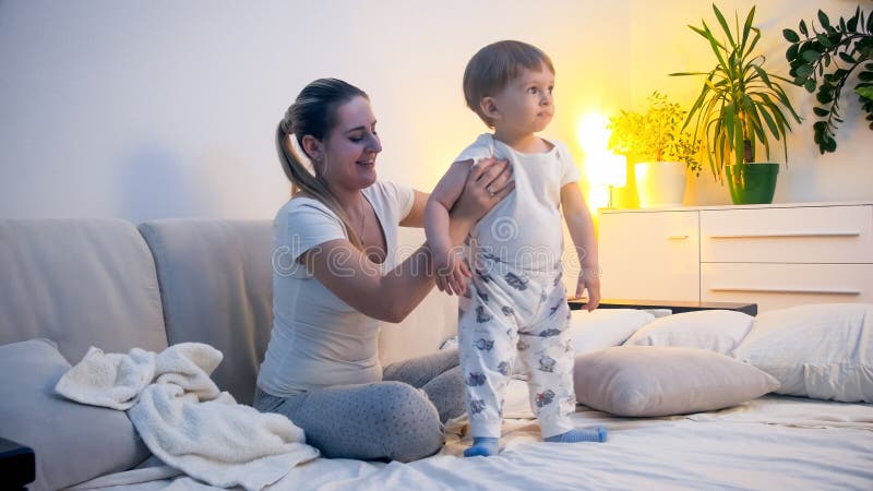 Gullig litet barnpojke i pyjamas med den unga le modern i säng, innan att gå att sova arkivbilder