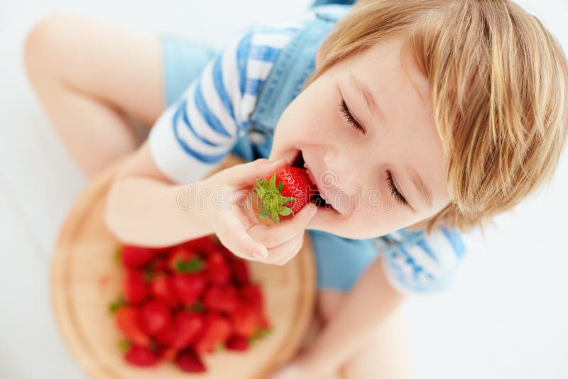 Cute happy kid, boy eating tasty ripe strawberries. Cute happy kid, boy eating tasty ripe strawberries