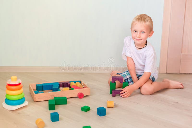 Gullig pys som spelar med kulöra träkvarter i rummet Tidigt utvecklingsbegrepp