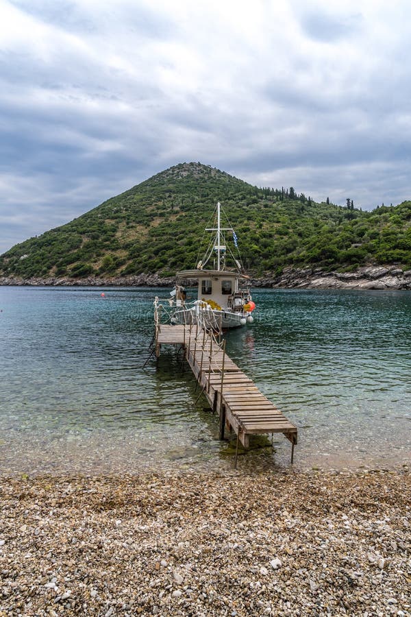 Gullig strandsikt in mot en bro som leder till ett litet fartyg, Sarakiniko strand, Ithaca ö, Grekland royaltyfri foto Gullig strandsikt in mot en bro som leder till ett litet fartyg, Sarakiniko strand, Ithaca ö, Grekland royaltyfri foto