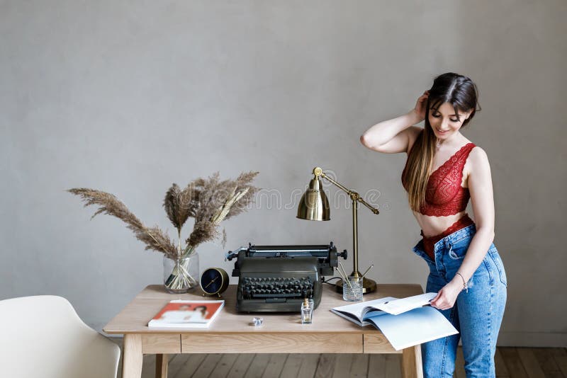 Gullig ung flicka - brunett i h?rlig underkl?der och jeans som st?r p? skrivbordet royaltyfria bilder Gullig ung flicka - brunett i h?rlig underkl?der och jeans som st?r p? skrivbordet royaltyfria bilder