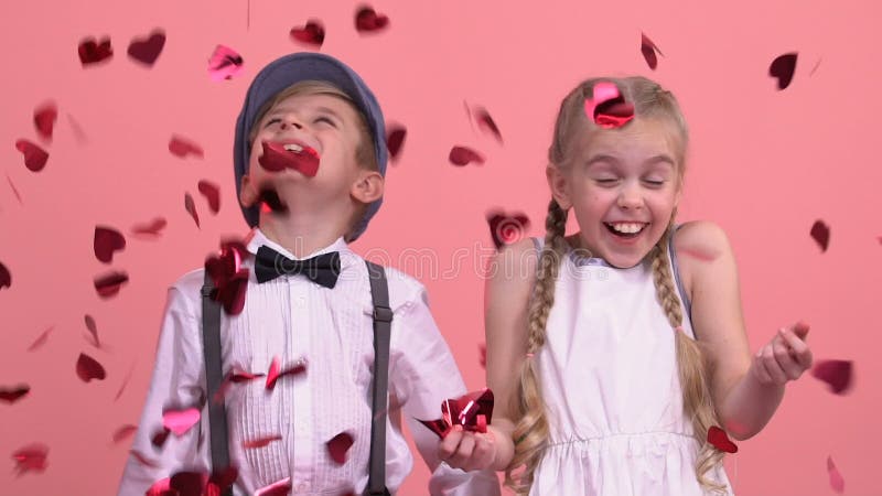 Gulliga barn som tycker om regn från ljusa hjärta-formade konfettier, St-valentindag