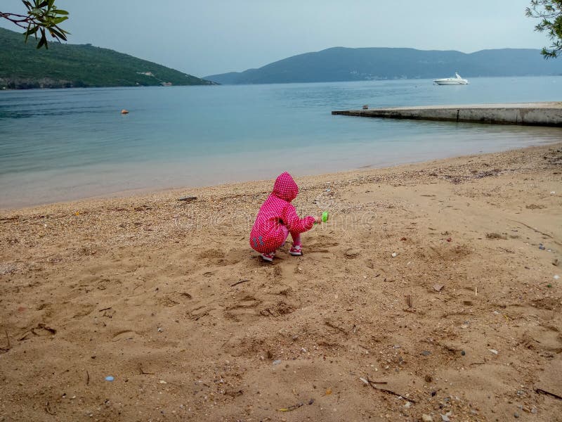 Gulliga små behandla som ett barn flickan som spelar med sanden på stranden i ett stormigt väder arkivfoto Gulliga små behandla som ett barn flickan som spelar med sanden på stranden i ett stormigt väder arkivfoto