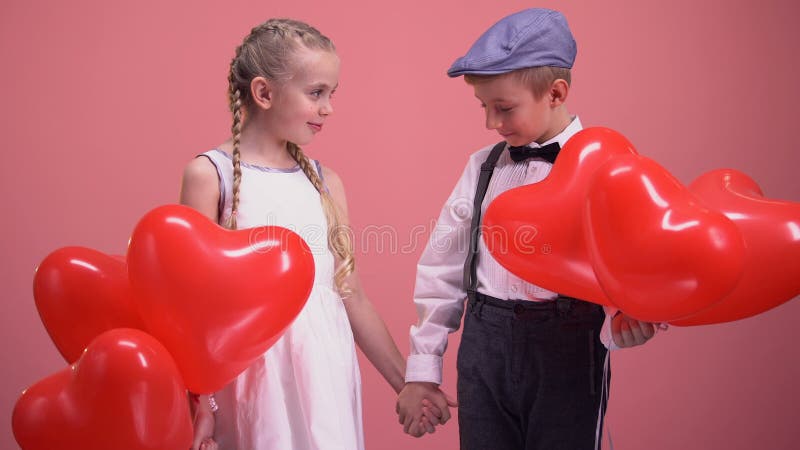 Gulliga små par med ballonger som rymmer händer och ler, ungar på förälskelsedatum