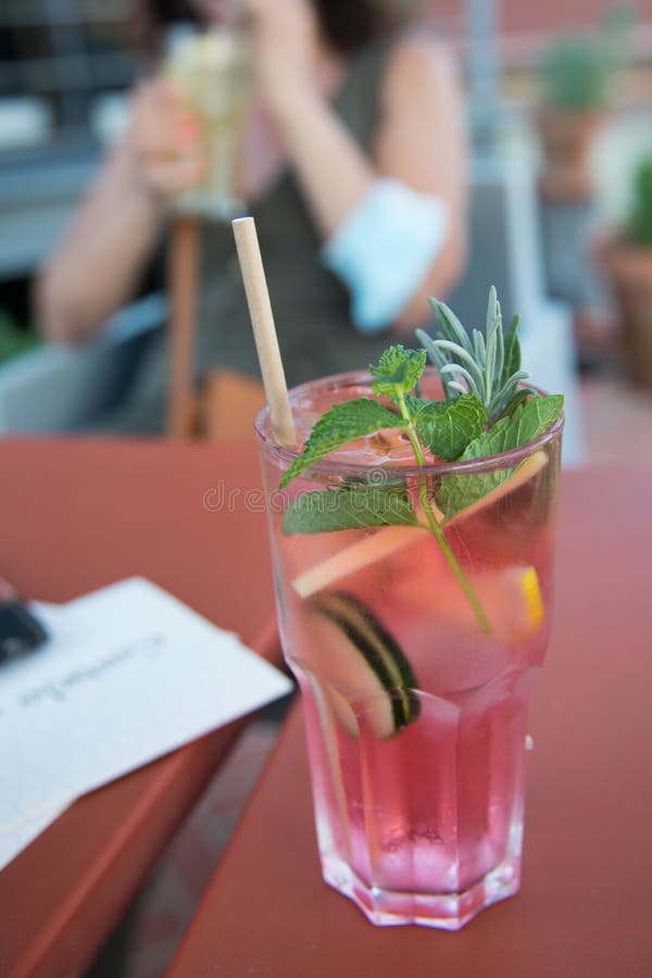 Gurkvatten med bär och citronsegment med rosa färg och kardbordsstrå. kvinna i bakgrunden med annat glas royaltyfri foto
