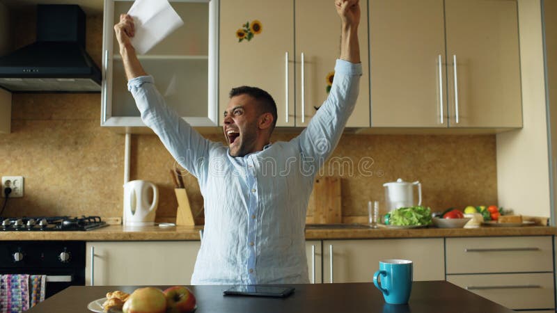 Gut aussehender Mann erhalten Brief der guten Nachrichten Lesein der Küche, während frühen Morgen des Frühstücks zu Hause haben S lizenzfreie stockbilder Gut aussehender Mann erhalten Brief der guten Nachrichten Lesein der Küche, während frühen Morgen des Frühstücks zu Hause haben S lizenzfreie stockbilder
